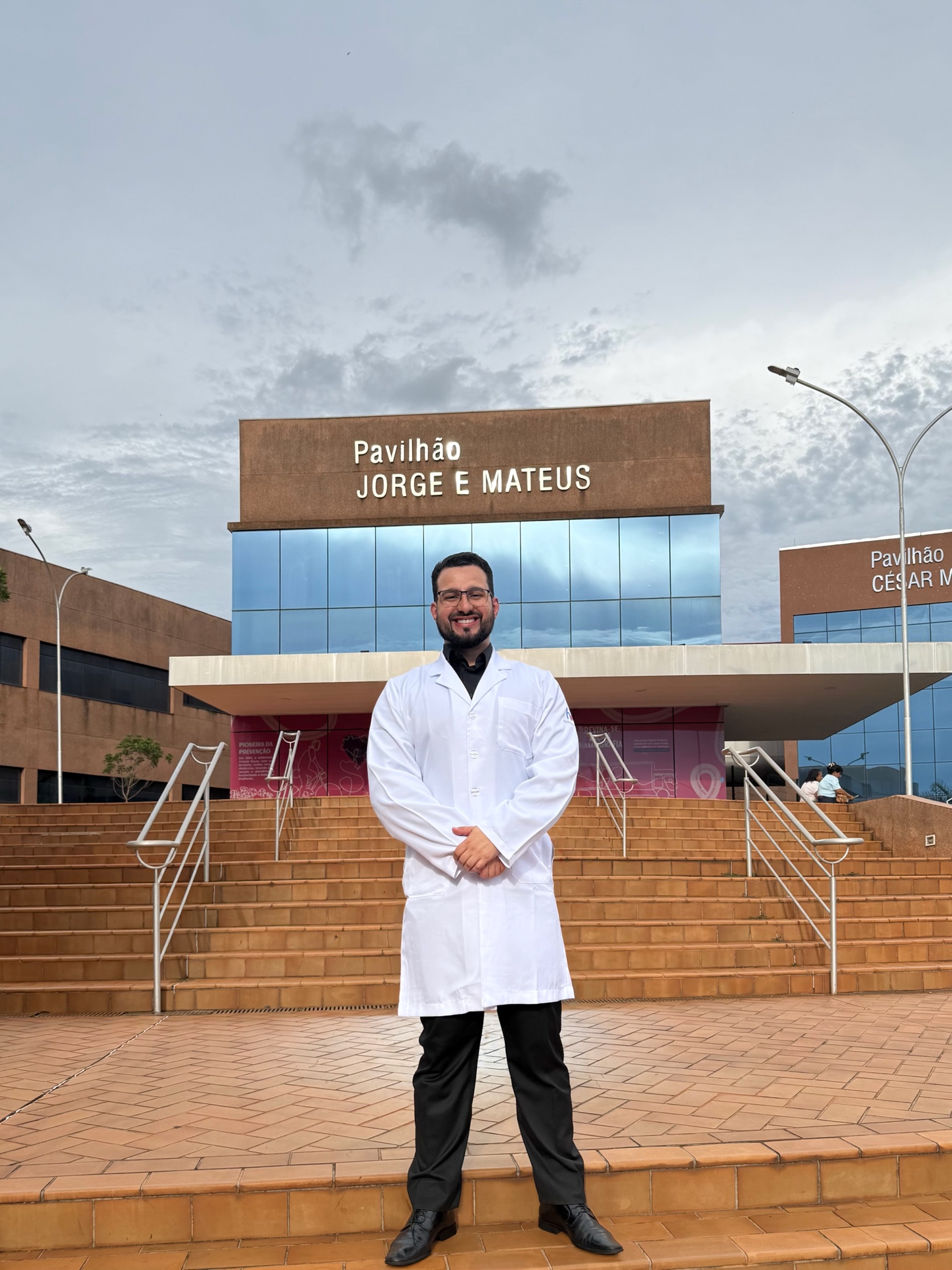 Dr. Samuel Drumond de jaleco em frente à escadaria de uma unidade hospitalar